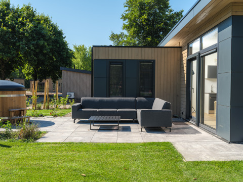 Udendørs opholdsområde med moderne sofa og bord ved Essenburgh Deluxe Lodge med spabad i Holland.