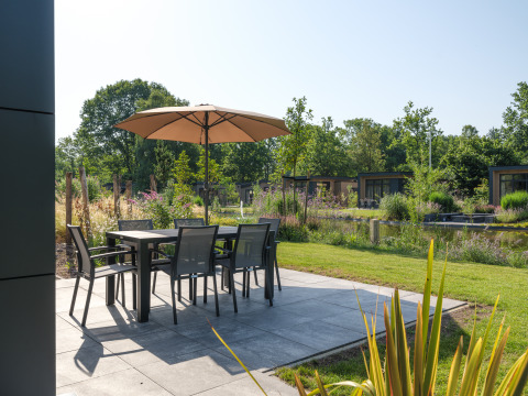Terrasse mit Tisch, Stühlen und Sonnenschirm bei der Essenburgh Comfort-Lodge im Veluwepark de Bosgraaf.