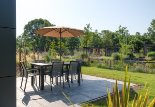 Terraza con mesa, sillas y sombrilla en la lodge Essenburgh Comfort en Veluwepark de Bosgraaf, Países Bajos.