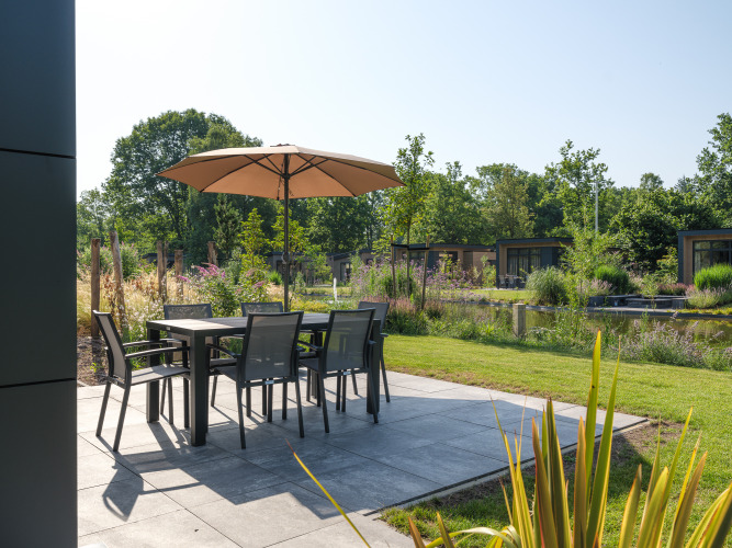 Terraza con mesa, sillas y sombrilla en la lodge Essenburgh Comfort en Veluwepark de Bosgraaf, Países Bajos.