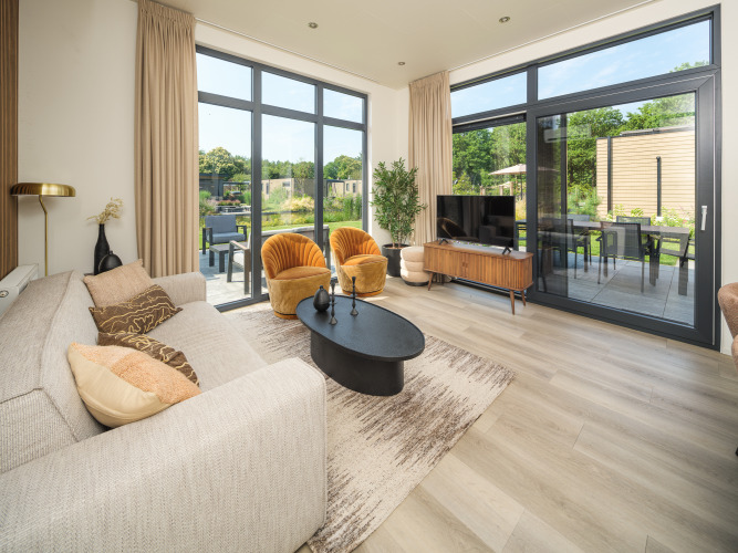 Salón de lodge moderno con grandes ventanales, sillones amarillos, sofá beige y vista al jardín y terraza.