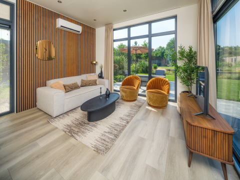 Modernes Lodge-Wohnzimmer mit großen Fenstern, beiger Couch, gelben Sesseln und Holzakzenten.