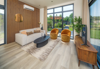 Modernes Lodge-Wohnzimmer mit großen Fenstern, beiger Couch, gelben Sesseln und Holzakzenten.