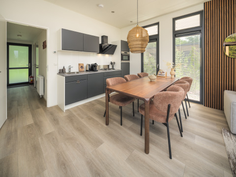 Cocina y comedor modernos en la cabaña, con mesa de madera, seis sillas cómodas y grandes ventanales.