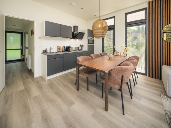 Cocina y comedor modernos en la cabaña, con mesa de madera, seis sillas cómodas y grandes ventanales.