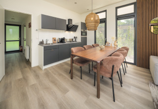 Cocina y comedor modernos en la cabaña, con mesa de madera, seis sillas cómodas y grandes ventanales.