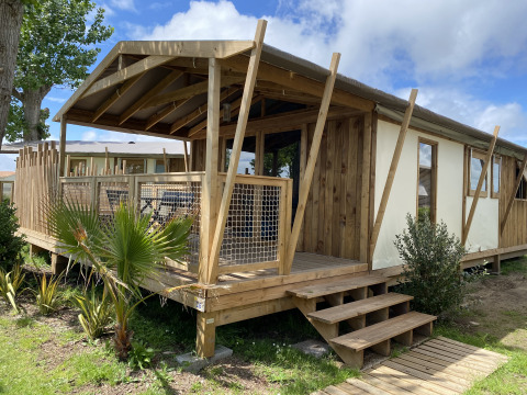 Cabaña de madera con terraza en Flower Camping Le Pré des Sables, parque vacacional en Pays de la Loire, Francia.