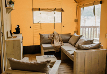 Intérieur de la tente safari Ranger Lodge au Veluwepark de Bosgraaf avec canapés en bois et coussins gris.