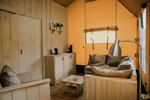 Binnenzicht van de Ranger Lodge safaritent op Veluwepark de Bosgraaf met houten meubels en sofa.