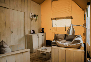 Innenansicht des Ranger Lodge Safari-Zeltes im Veluwepark de Bosgraaf mit Holzmöbeln und Sofa.