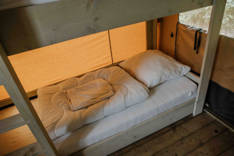 Een eenpersoonsbed met wit beddengoed in een safaritent van Ranger Lodge, Veluwepark de Bosgraaf, Nederland.