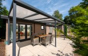 Überdachte Terrasse mit Gartenmöbeln vor der Veluwe Lodge im Veluwepark de Bosgraaf in den Niederlanden.
