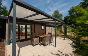 Terrasse couverte avec table et chaises à la Veluwe Lodge du Veluwepark de Bosgraaf, entourée de verdure.