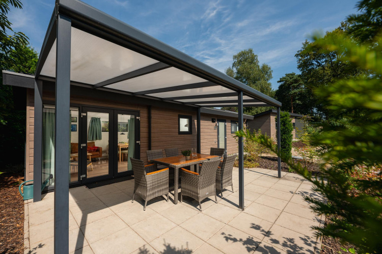 Überdachte Terrasse mit Gartenmöbeln vor der Veluwe Lodge im Veluwepark de Bosgraaf in den Niederlanden.