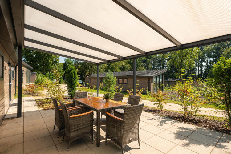 Überdachte Terrasse der Veluwe Lodge im Veluwepark de Bosgraaf, Niederlande, mit Esstisch und Stühlen.