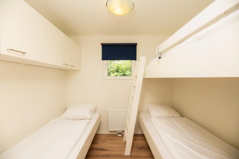 Room with two single beds, bunk bed, cabinets, and window at Veluwe Lodge in Veluwepark de Bosgraaf, Netherlands.