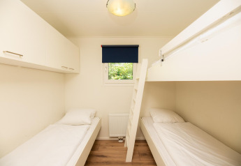Habitación con dos camas individuales, litera, armarios y ventana en Veluwe Lodge, Veluwepark de Bosgraaf, Países Bajos.