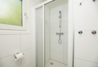 Doccia minimalista con piastrelle bianche, finestra e ganci alla Veluwe Lodge nei Paesi Bassi.