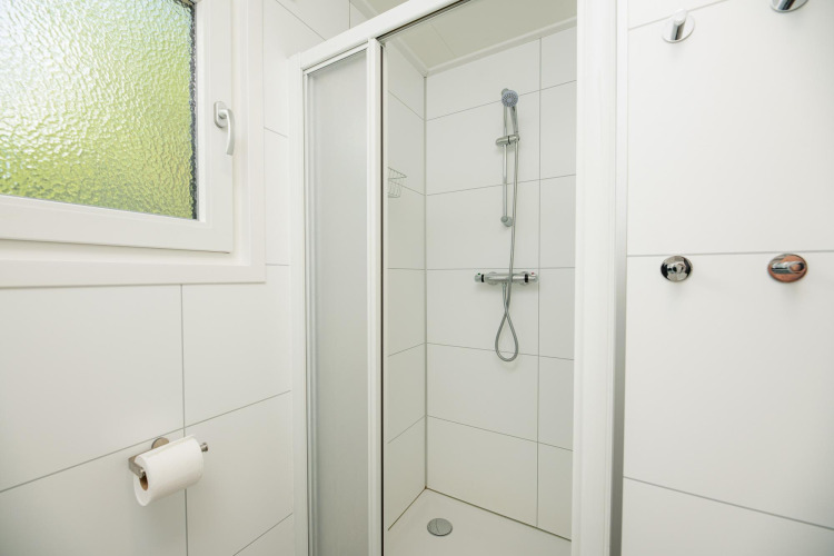 Moderne Duschkabine mit weiß gefliesten Wänden, Fenster und Haken in der Veluwe Lodge, Niederlande.