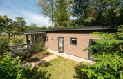 Moderne Waldhütte im Veluwepark de Bosgraaf, Niederlande, mit Garten und umgeben von Bäumen im Sommer.