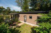 Moderne Waldhütte im Veluwepark de Bosgraaf, Niederlande, mit Garten und umgeben von Bäumen im Sommer.