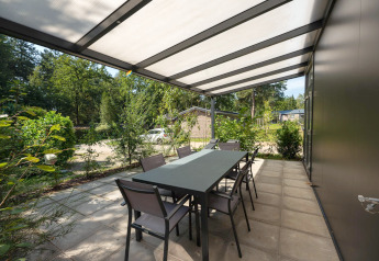 Udendørs terrasse med bord og stole på Forest Lodge ved Veluwepark de Bosgraaf, omgivet af natur.