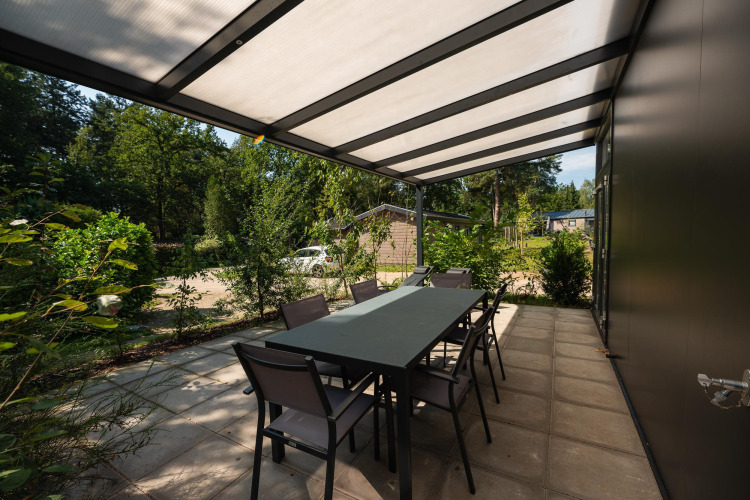 Covered outdoor patio with table and chairs at Forest Lodge in Veluwepark de Bosgraaf, Netherlands.