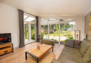 Lys stue i Forest Lodge, Veluwepark de Bosgraaf, Holland, med store vinduer og udsigt til haven.