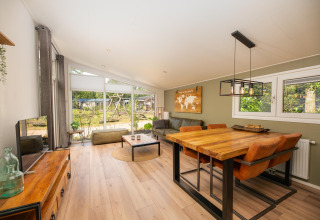 Lys, moderne stue og spisestue i Forest Lodge ved Veluwepark de Bosgraaf, Holland, med store vinduer.