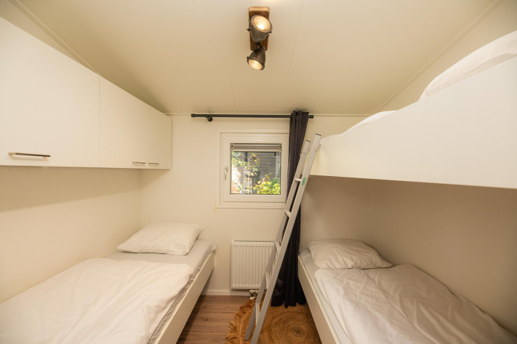 Helles Schlafzimmer mit Einzelbetten und Etagenbett in der Forest Lodge im Veluwepark de Bosgraaf, Niederlande.