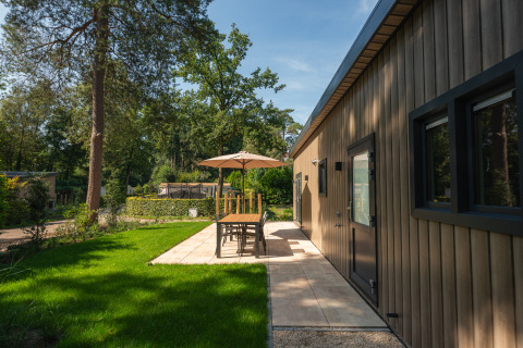 Außensitzbereich einer Lodge im Veluwepark de Bosgraaf, Niederlande, mit Sonnenschirm und Grünfläche.