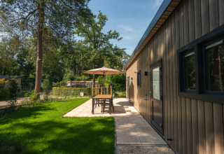 Außensitzbereich einer Lodge im Veluwepark de Bosgraaf, Niederlande, mit Sonnenschirm und Grünfläche.