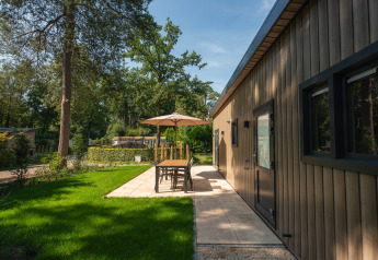 Patio esterno accanto a un lodge al Veluwepark de Bosgraaf nei Paesi Bassi, circondato da alberi e prato.
