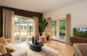 Modern lodge living room with large windows, beige curtains, black furnishings, and garden view.