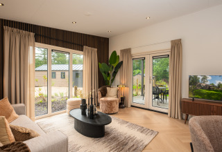 Moderne lodge-stue med store vinduer, beige gardiner, sorte møbler og udsigt til grøn have.