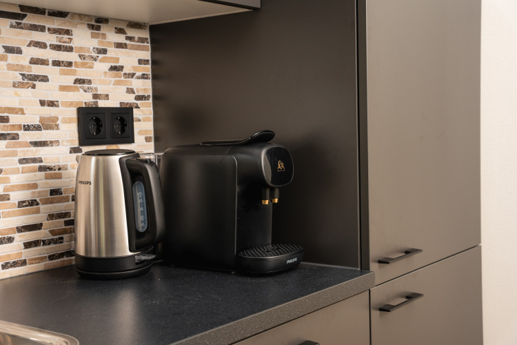 Kaffeemaschine und Wasserkocher auf schwarzer Arbeitsplatte vor Mosaikfliesen in einer Lodgeküche.