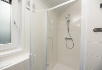 Ducha moderna con azulejos blancos y puerta de cristal en Lodge Loevestein, Veluwepark de Bosgraaf, Países Bajos.
