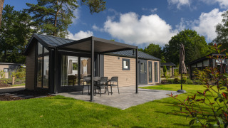 Moderne glampingaccommodatie met terras, tuinset en grasveld, omringd door natuur en bomen.
