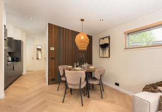 Spiseområde i moderne lodge med trævæg, hyggelig belysning og vindue med udsigt til haven.