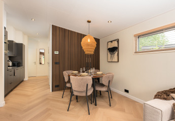 Coin repas dans un lodge moderne avec mur en bois, lumière chaleureuse et fenêtre sur l'extérieur.