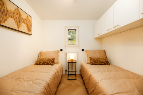Chambre lumineuse de lodge avec deux lits simples, parure beige, petite fenêtre et décor minimaliste.
