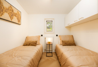 Chambre lumineuse de lodge avec deux lits simples, parure beige, petite fenêtre et décor minimaliste.