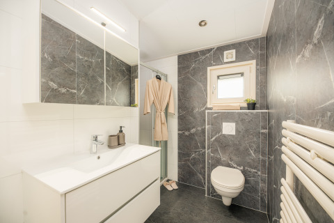 Baño moderno de lodge con azulejos de mármol gris, inodoro suspendido y bata colgada cerca de la ducha.