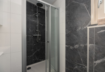 Cabina de ducha moderna con puertas de vidrio y paredes estilo mármol oscuro en baño de lodge con ventana.