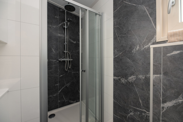 Moderne Duschkabine mit Glastüren und dunklen Marmorwänden in einem Lodge-Badezimmer mit Fenster.