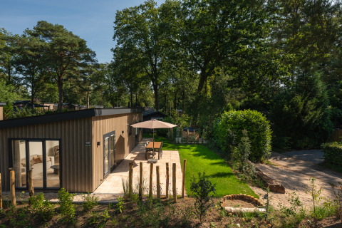 Moderne lodge Loevestein med boblebad og terrasse ved Veluwepark de Bosgraaf, omgivet af grønne træer.