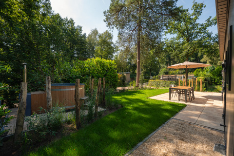 Tuin met hottub en terras aan Loevestein-lodge in Veluwepark de Bosgraaf, Nederland, met bomen rondom.