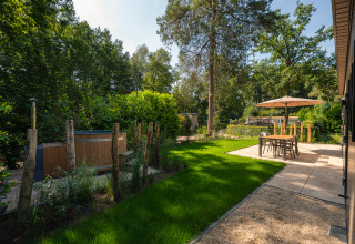 Tuin met hottub en terras aan Loevestein-lodge in Veluwepark de Bosgraaf, Nederland, met bomen rondom.