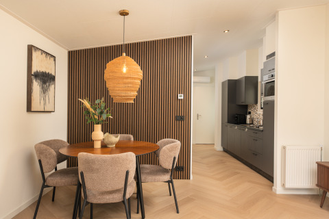 Comedor elegante con mesa redonda, cuatro sillas y cocina moderna en lodge de Veluwepark de Bosgraaf.