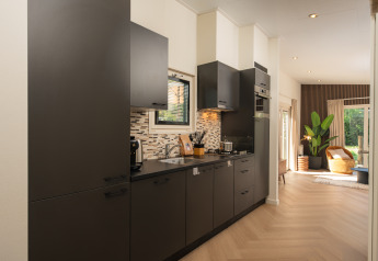 Cucina moderna nella lodge Loevestein al Veluwepark de Bosgraaf, con mobili neri e vista sul soggiorno.